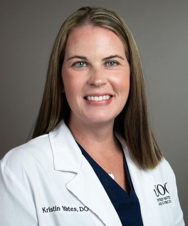 Kristin Yates, DO, smiling in a white lab coat, navy top, against a gray background.