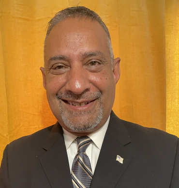 Man in suit and tie smiling, set against a yellow backdrop.