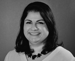 Smiling woman with dark hair wearing a white top and a dark necklace. Black and white photo.