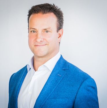 Man in blue blazer and white shirt smiles, headshot.