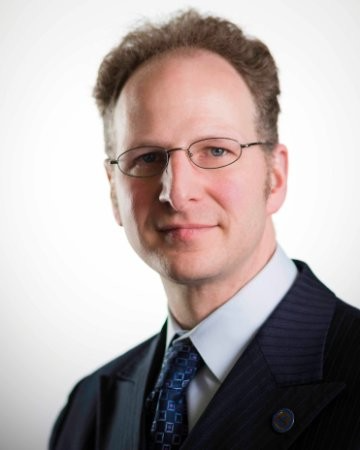Man in glasses and suit, smiling, looking at the viewer against a white background.