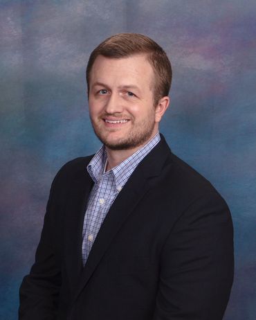 Man in blue shirt and blazer smiles, looking at the camera.