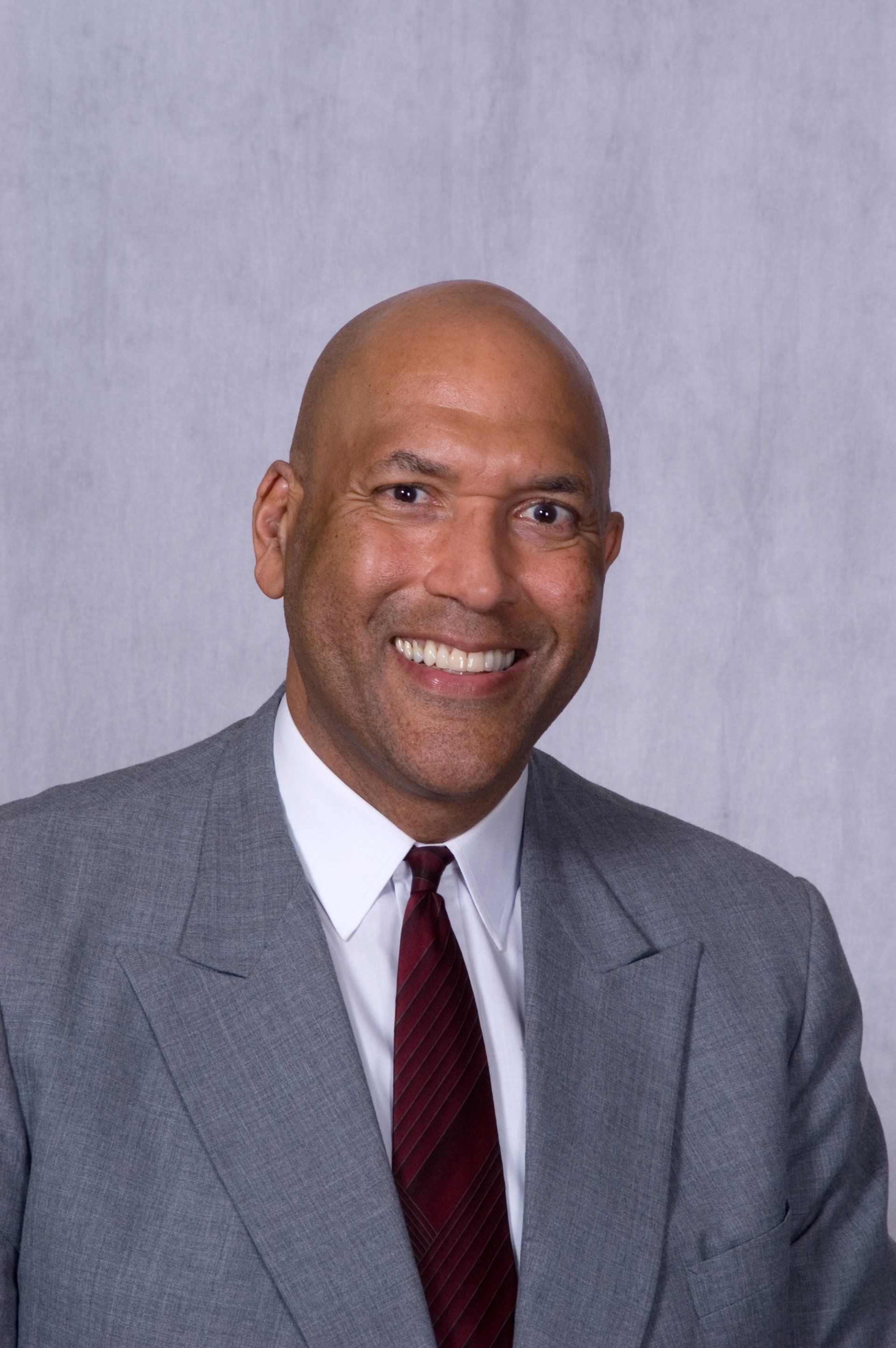 Man in gray suit and red tie smiles at the camera.