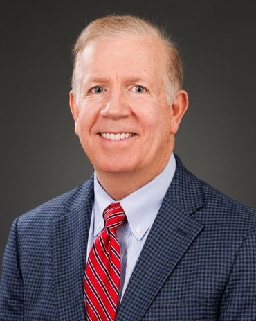 Man in a blue blazer and red tie, smiling against a gray background.