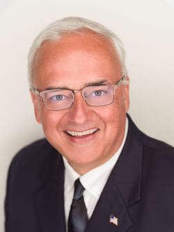 Man in glasses and suit smiles at the camera against a white background.