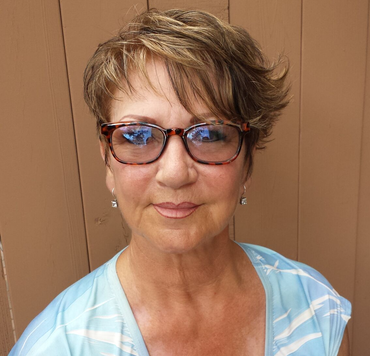 Woman with short brown hair and glasses smiling in front of a wood background.