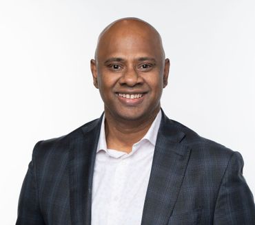Bald man in a dark blazer smiling, set against a white background.