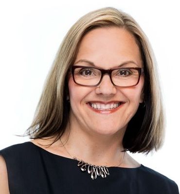 Woman wearing glasses smiles at the camera, wearing a black top and silver necklace.