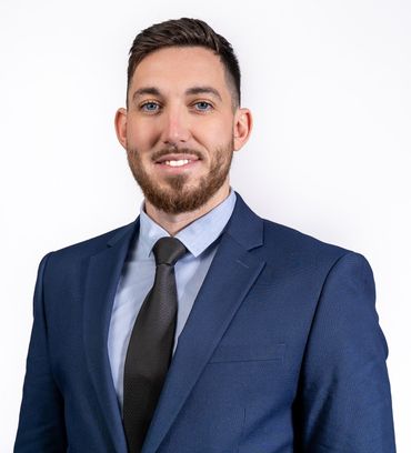 Man in blue suit, light blue shirt, and dark tie smiles against a white background.