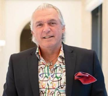 Man in suit jacket and colorful shirt, smiling, red pocket square.