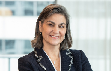 Woman in a dark blazer smiles at the camera, in an office setting.