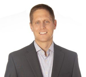 Man in suit jacket smiles at the camera, against a white background.