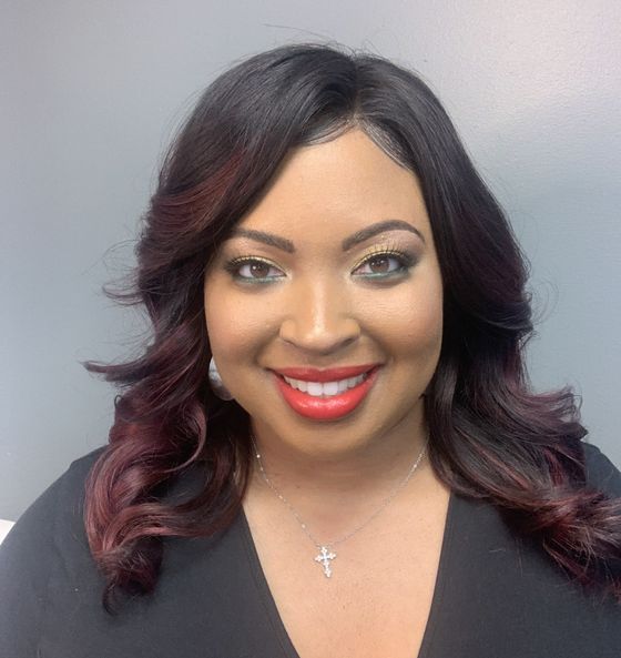 Woman with dark hair and red highlights, wearing makeup, smiling, and wearing a necklace.