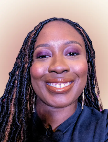 Woman with locs smiles, wearing purple eyeshadow and glossy lip. Beige background.