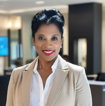 Woman in business attire smiling in an office setting, wearing a blazer and white shirt.