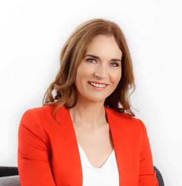 Woman in orange blazer smiles at the camera, indoors.