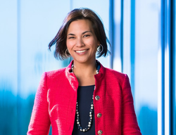 Woman in red jacket smiles in front of a blue background.