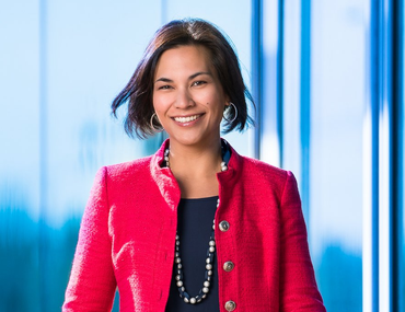 Woman in red jacket smiles in front of a blue background.