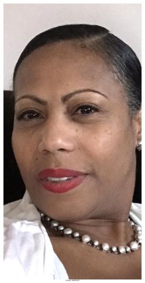 Woman with dark skin, wearing a white shirt and pearl necklace, red lipstick, looking at the camera.