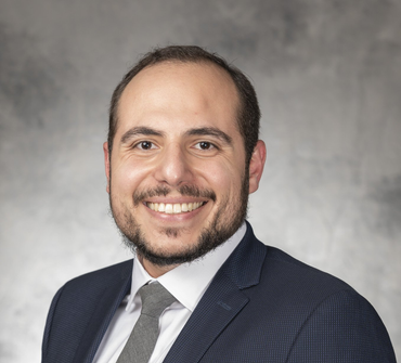 Man in a suit smiling, posing for a portrait against a gray background.