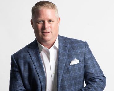 Man in blue plaid blazer and white shirt, smiling, looking at the camera.