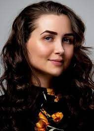 Woman with dark curly hair and a floral shirt smiles, looking slightly to the side.