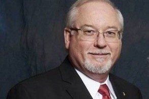 Man in glasses, suit, and red tie, smiling.