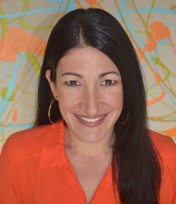 Woman with dark hair smiles, wearing an orange shirt and gold hoop earrings. Background: colorful abstract art.