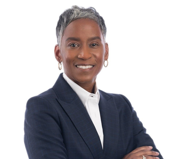 Smiling person in a dark suit, arms crossed, white background.