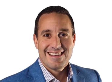 Man in blue blazer smiling, headshot against white background.