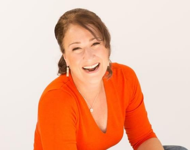Woman in orange shirt laughs, white background.