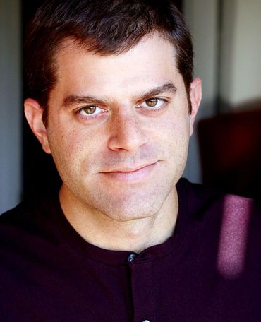 Man with brown hair, smiling slightly, wearing a dark purple shirt.