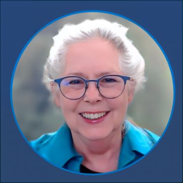 Smiling woman with white hair wearing blue glasses and a teal top.