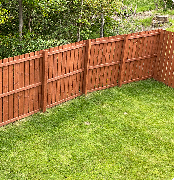 a wooden fence surrounds a lush green lawn in a backyard .