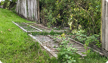 a broken wooden fence is sitting in the grass next to a wooden fence .