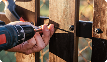 a person is using a drill to fix a wooden fence .