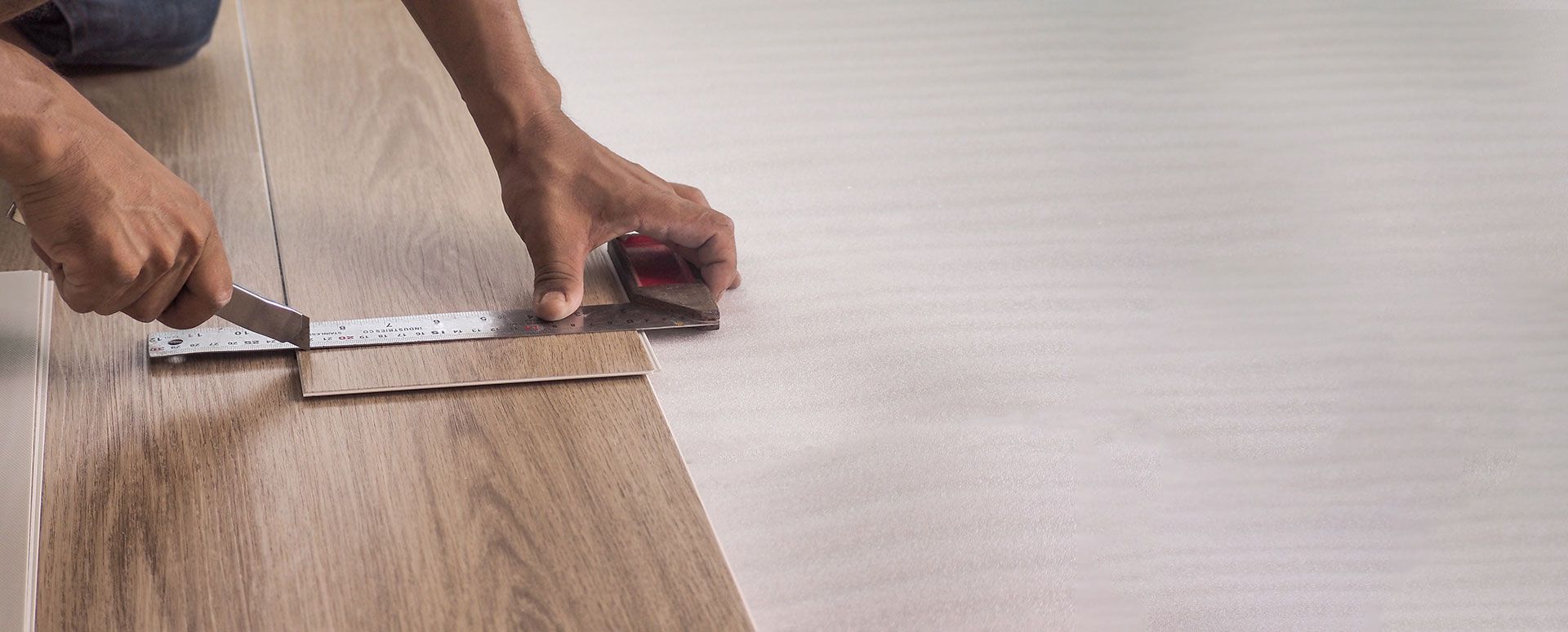 A person is measuring a piece of vinyl plank with a tape measure.