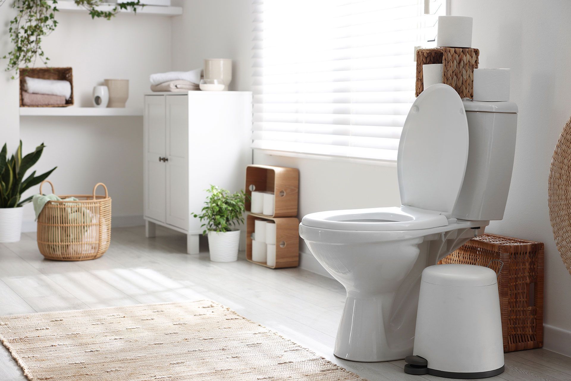 A bathroom with a toilet , trash can , and rug.