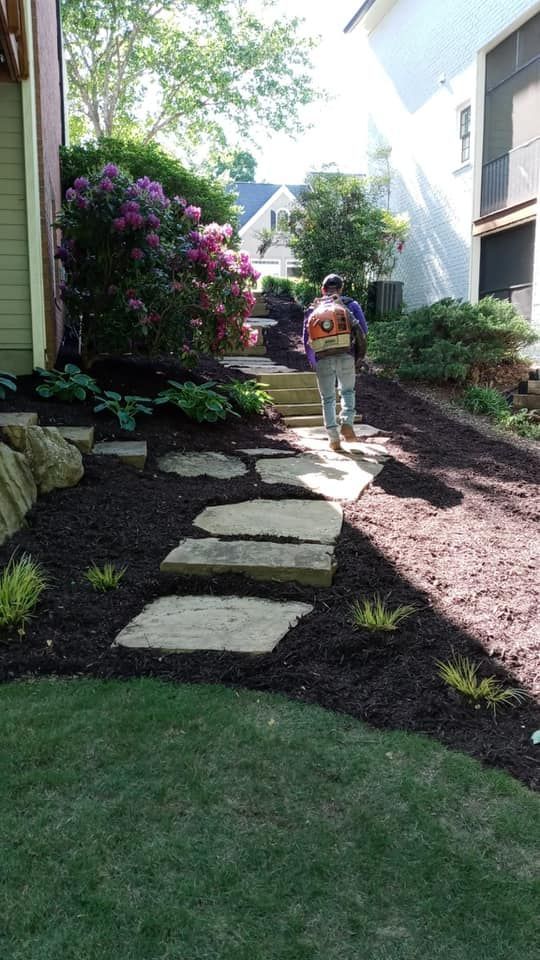 Person using a leaf blower on a landscaped pathway with stone steps and mulch.