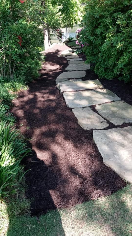 Stone path winding through a garden, lined with mulch, greenery, and trees.