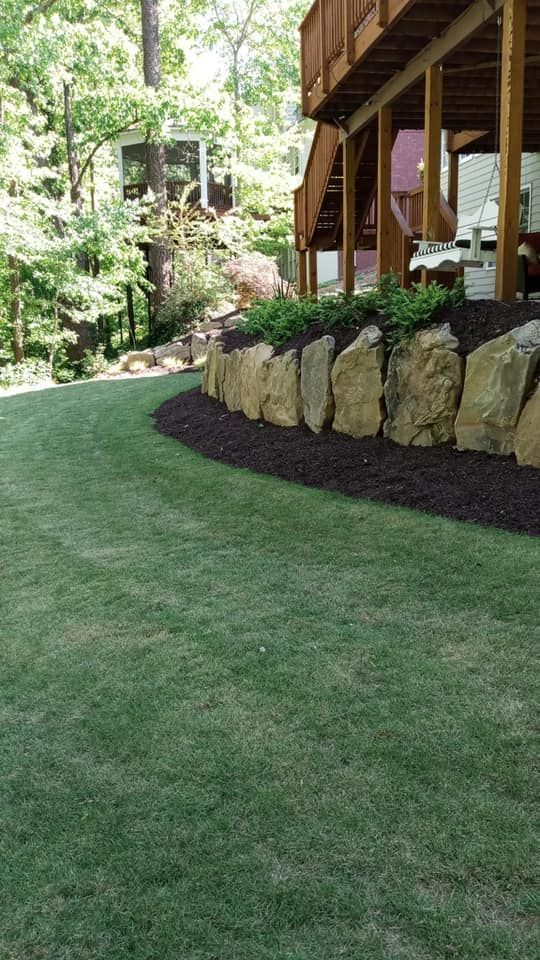Green lawn, rock retaining wall with plants, and wooden deck.