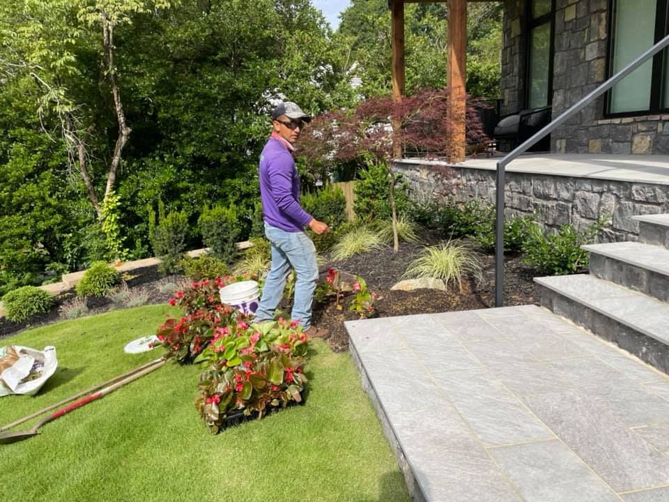 Man planting flowers in a landscaped yard next to stone steps and a house.