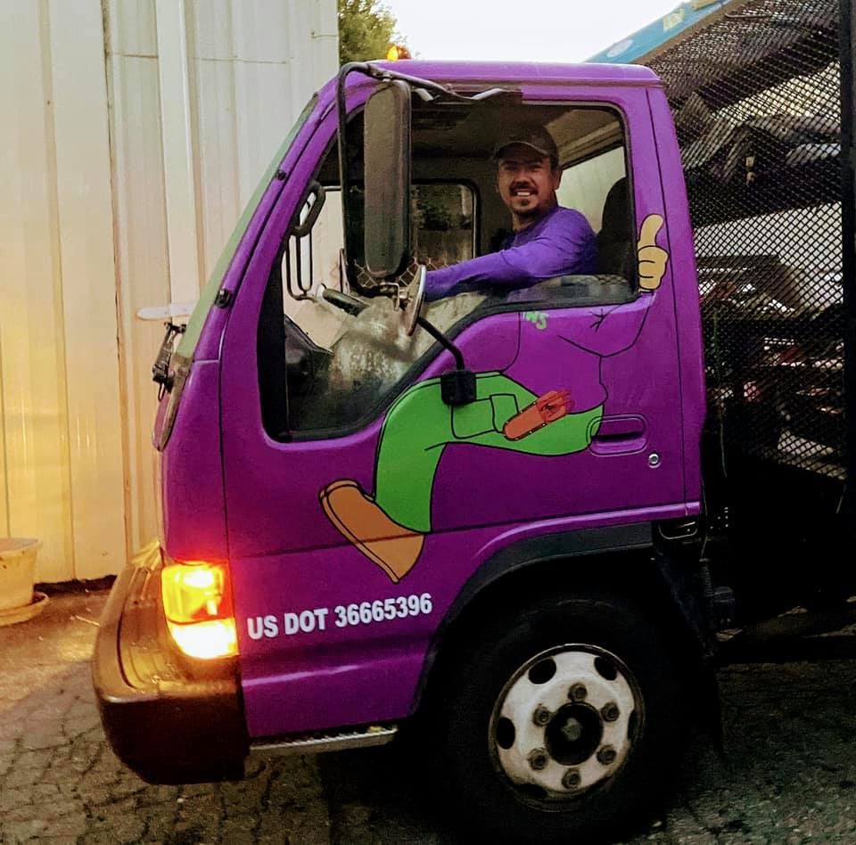 Man in a purple truck with a cartoon character, giving a thumbs-up.