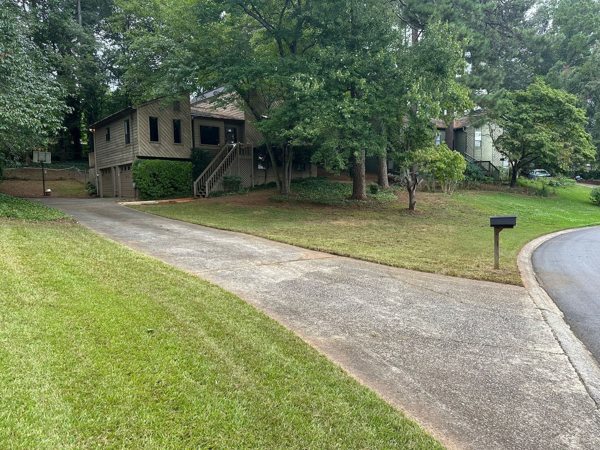 Driveway leading to a house, with green lawn and trees. A mailbox is visible.