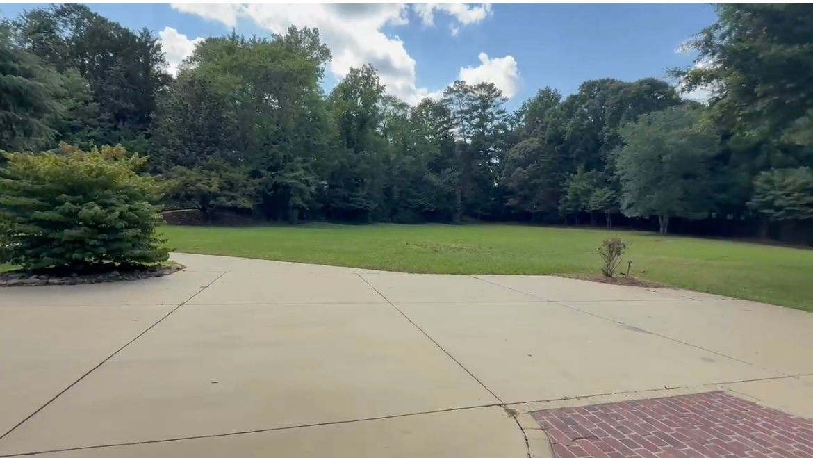 Concrete patio leads to a grassy yard and treeline under a blue sky.