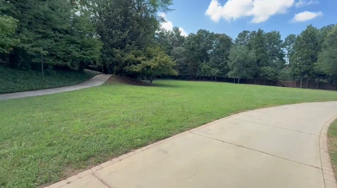 Grassy lawn with paved path, trees, and blue sky.