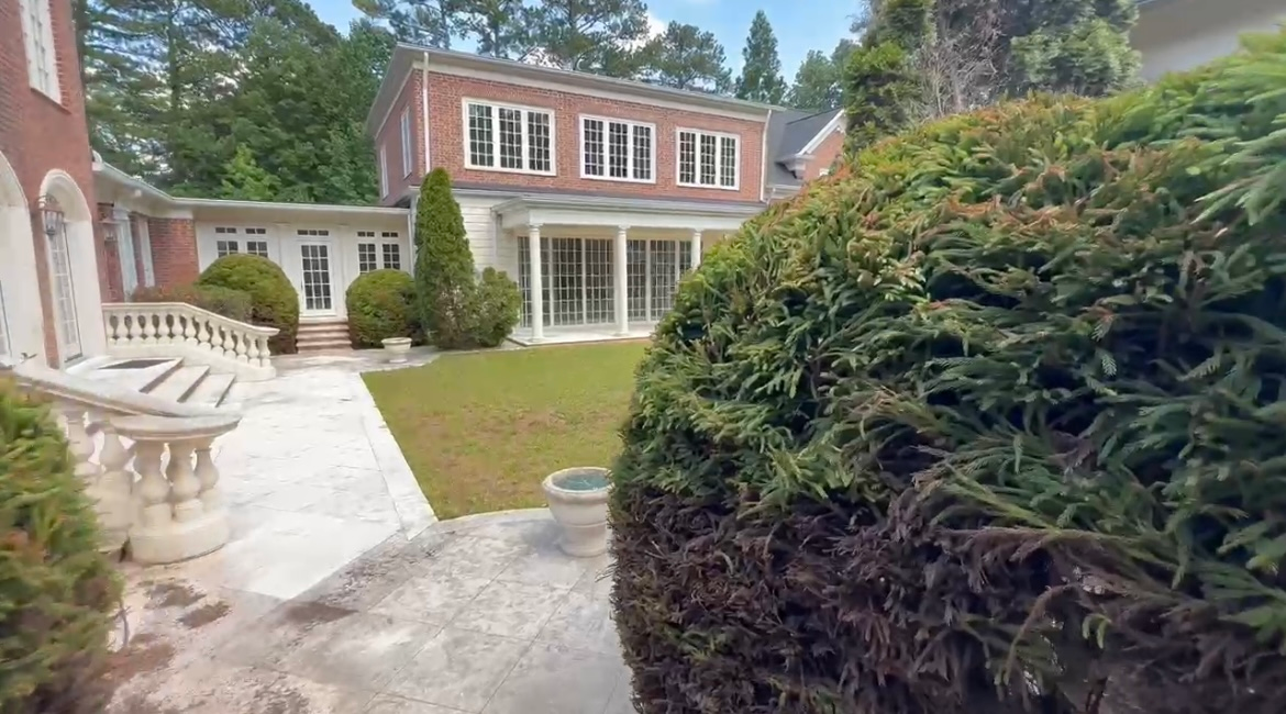 Exterior of a large brick house with a green lawn, shrubbery, and a paved walkway.