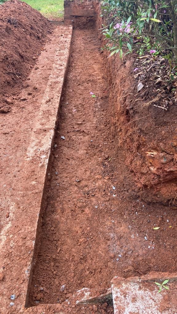 A long, narrow trench dug into reddish-brown earth; a step at the end.