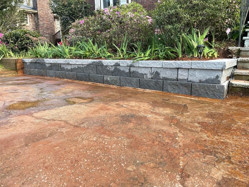 A low retaining wall of dark gray stone bordering a garden bed, set in front of a house.