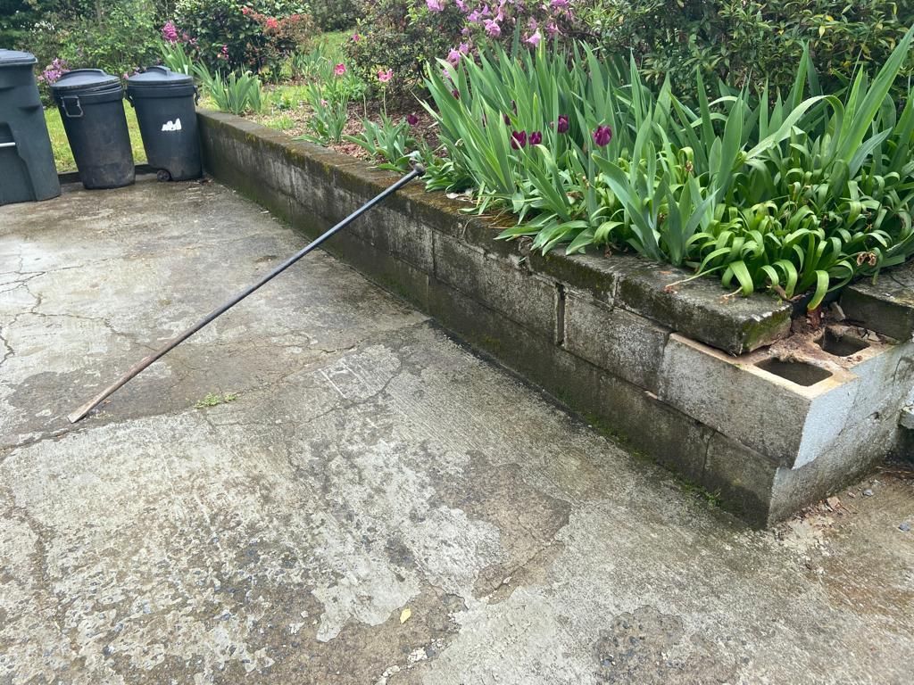 Concrete patio with raised garden bed.  Black trash cans on left. Fishing pole rests on patio.